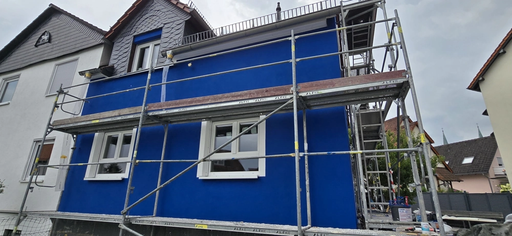 Hausfassade in leuchtendem Blau mit montiertem Gerüst bei Fassadendämmung