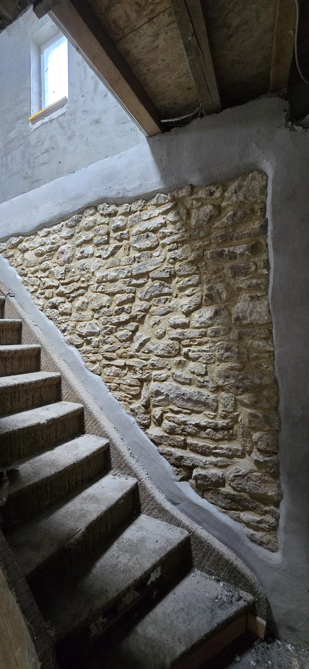 Betontreppe neben freigelegter Natursteinwand im Dachgeschossausbau