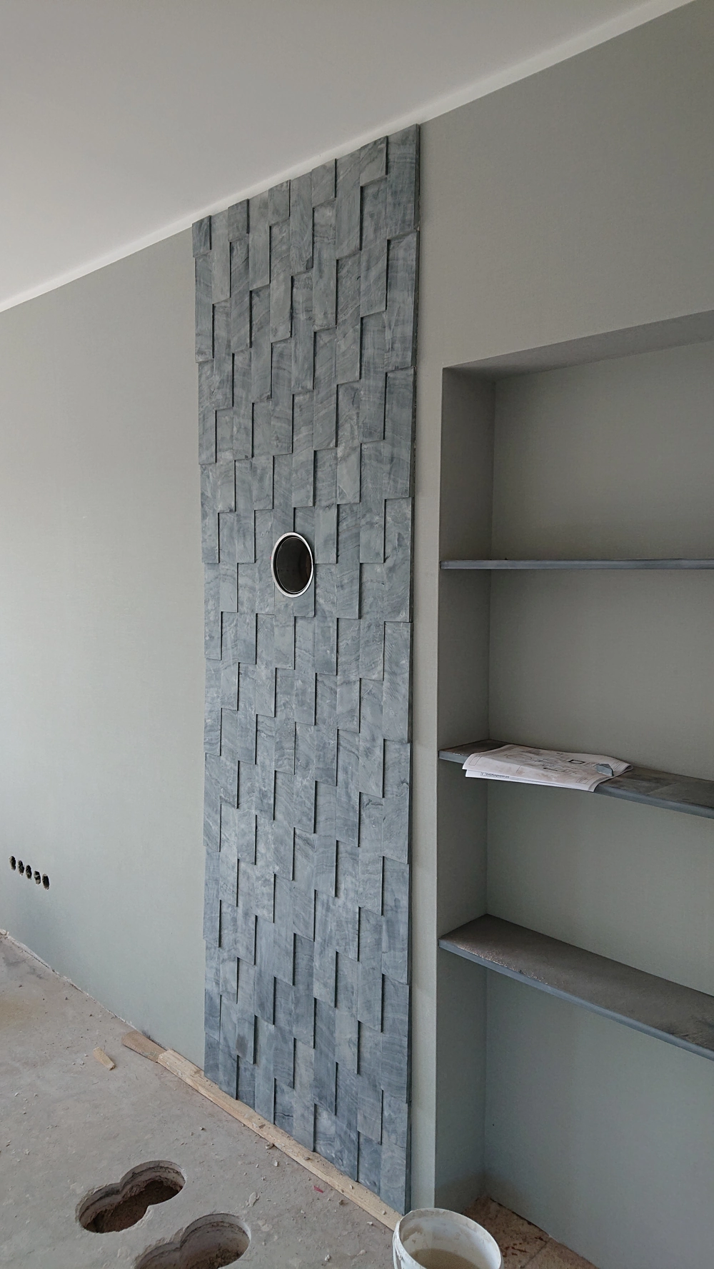 Graue Naturstein Wandverkleidung im Innenausbau mit rundem Ausschnitt für Steckdose und angrenzender Regalnische