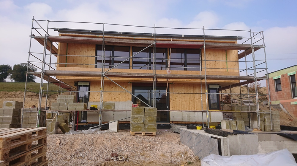 Gerüst vor zweigeschossigem Holzhaus mit Dämmplatten und Mauerarbeiten für Fassadendämmung