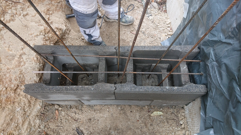 Aufgestapelte Betonblocksteine mit eingegossenem Bewehrungsstahl und frischem Betonfundament auf Baustelle
