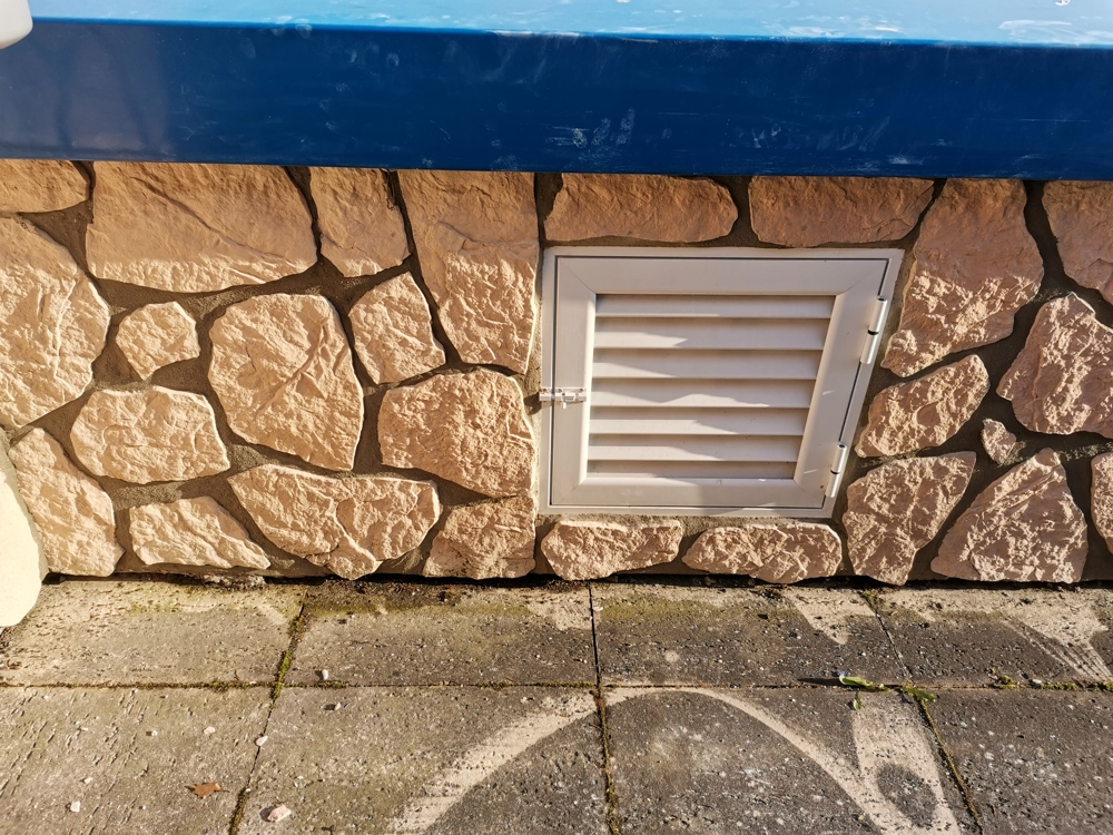 Naturstein Wandverkleidung mit Lüftungsgitter und gepflastertem Gehweg