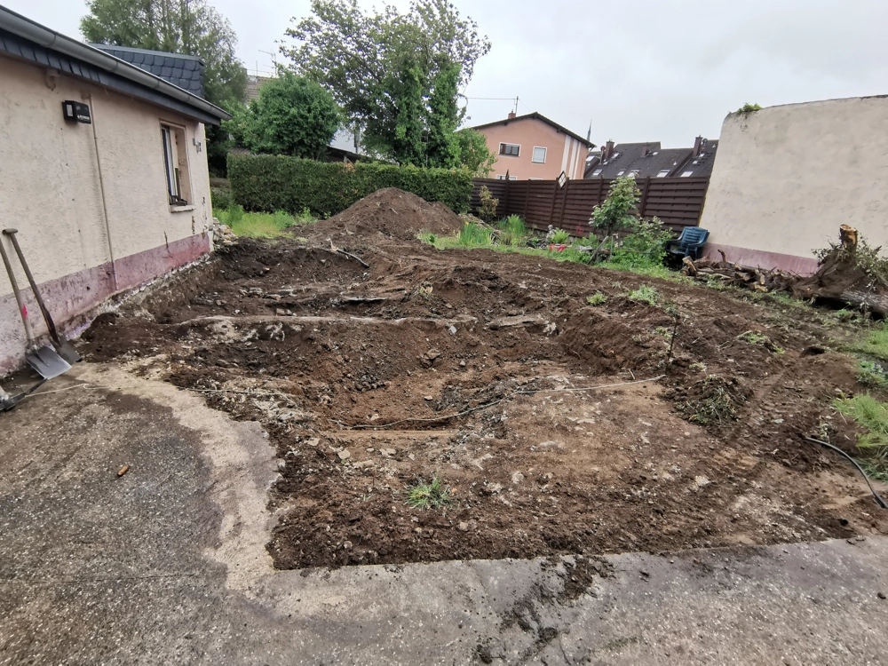 Aufgegrabener Gartenbereich mit Erdhügeln und Schaufeln neben Hauswand, Bodenarbeiten für Gartenanlage