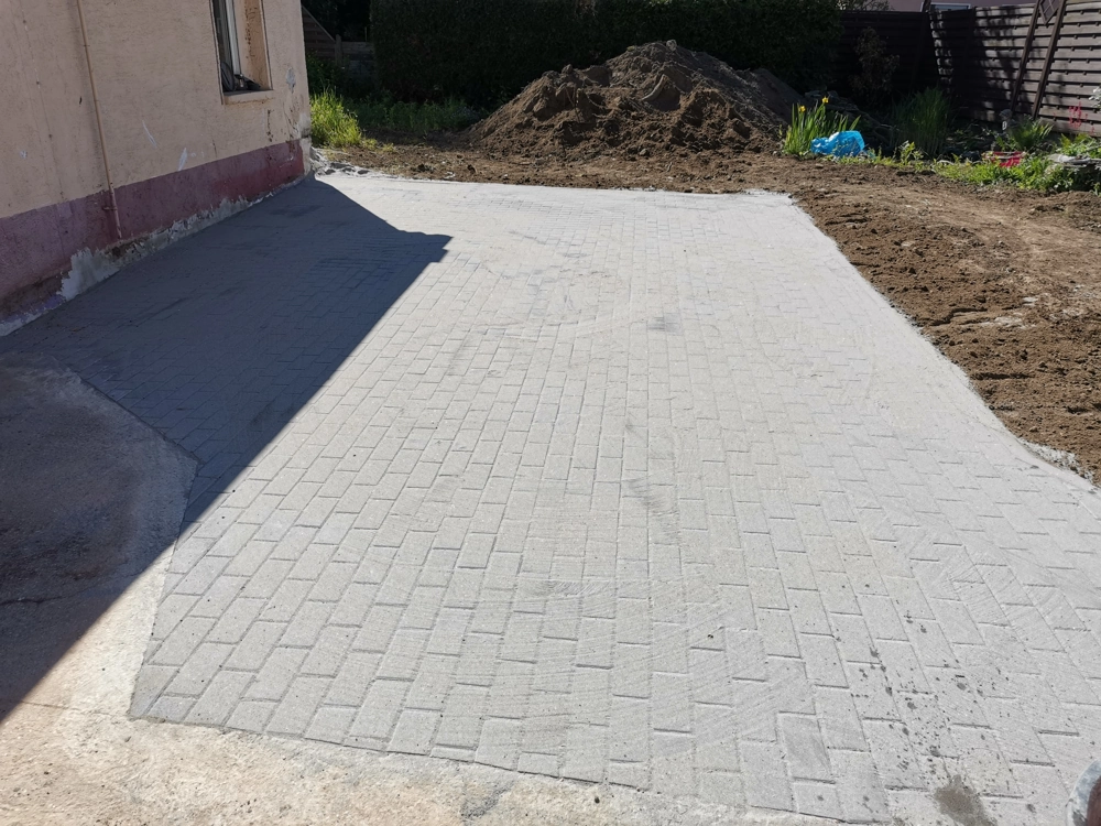 Einfahrt pflastern mit grauen Betonsteinen vor Hauswand und angrenzendem Erdwall