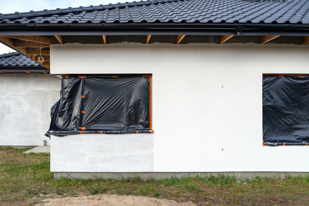 Hausfassade mit frischem Putz und abgeklemmten Fenstern im Zuge der Fassadendämmung