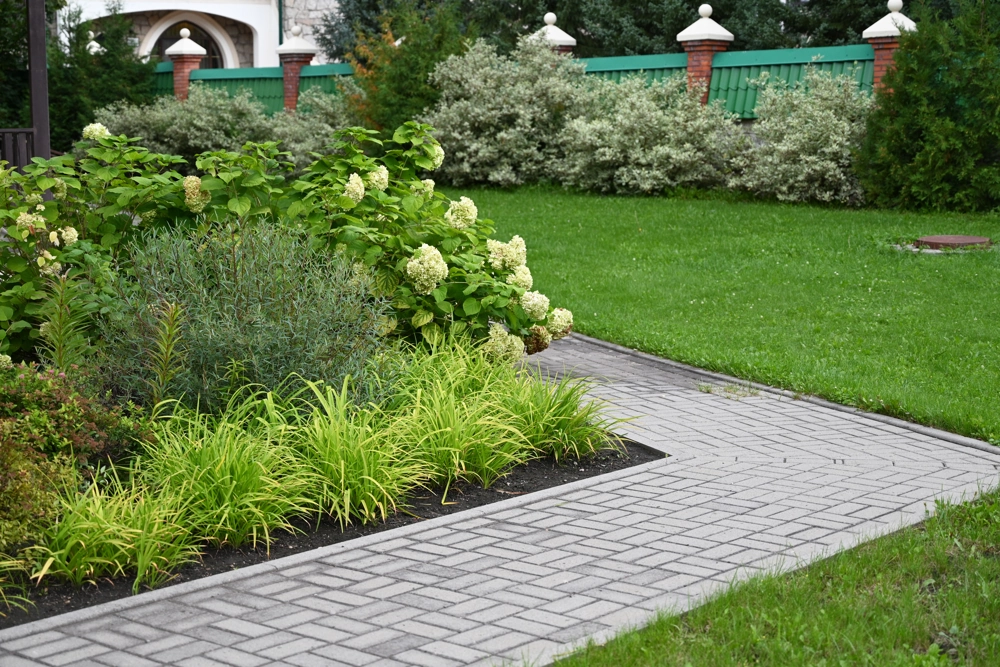 Gepflasterter Gartenweg neben Rasen und Blumenbeeten (Gehwege pflastern)