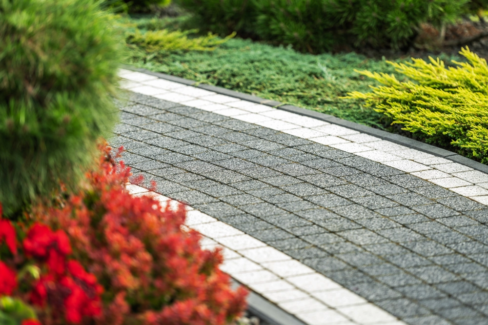 Geschwungener Gehweg mit grauen und weißen Pflastersteinen, umgeben von bunten Gartenpflanzen – Gehwege pflastern