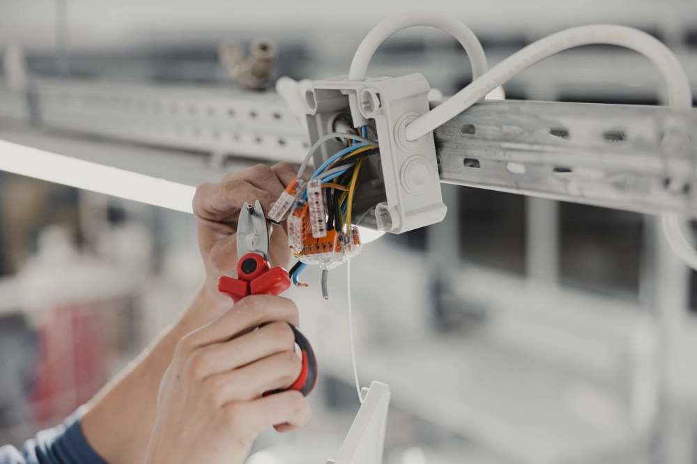 Hände verbinden bunte Kabel in offener Verteilerdose bei Elektroinstallation