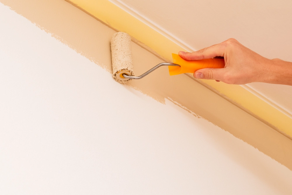 Malerarbeiten: Hand streicht Innenwand nahe Decke mit Farbrolle