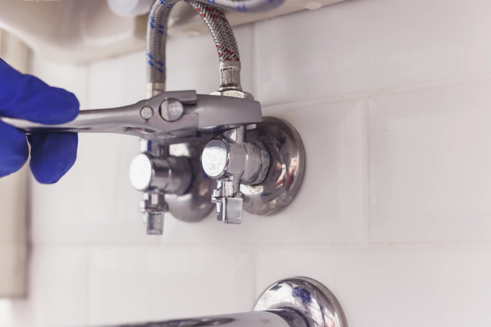 Sanitärinstallation: Fachmann zieht Eckventil unter Waschbecken mit Zange fest