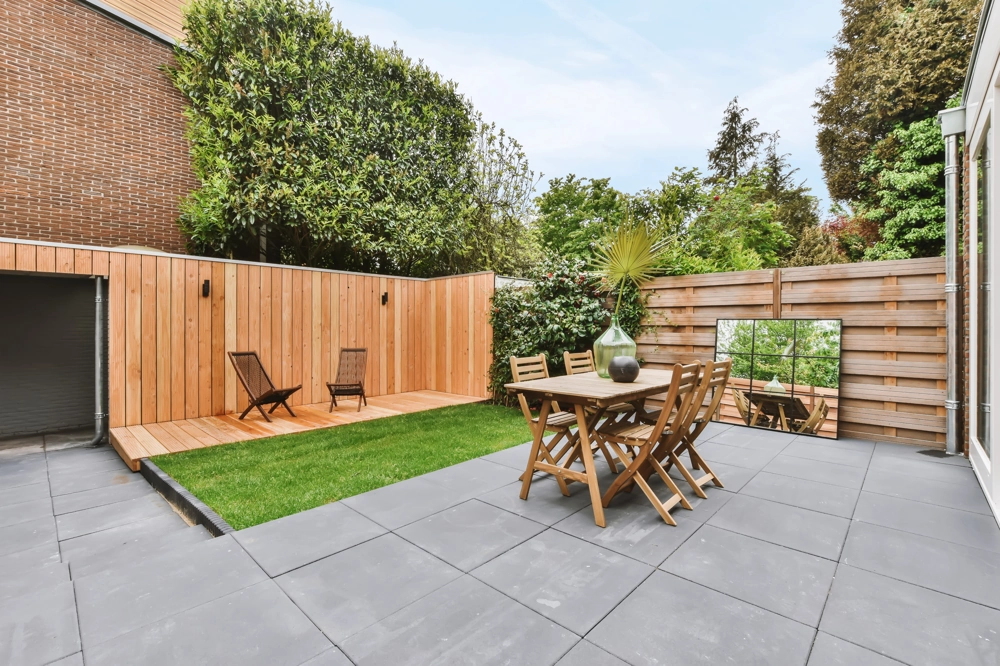 Gepflasterte Terrasse mit grauen Platten, Holz-Sitzgarnitur, angrenzendem Rasen und Holzzaun, Terrasse pflastern