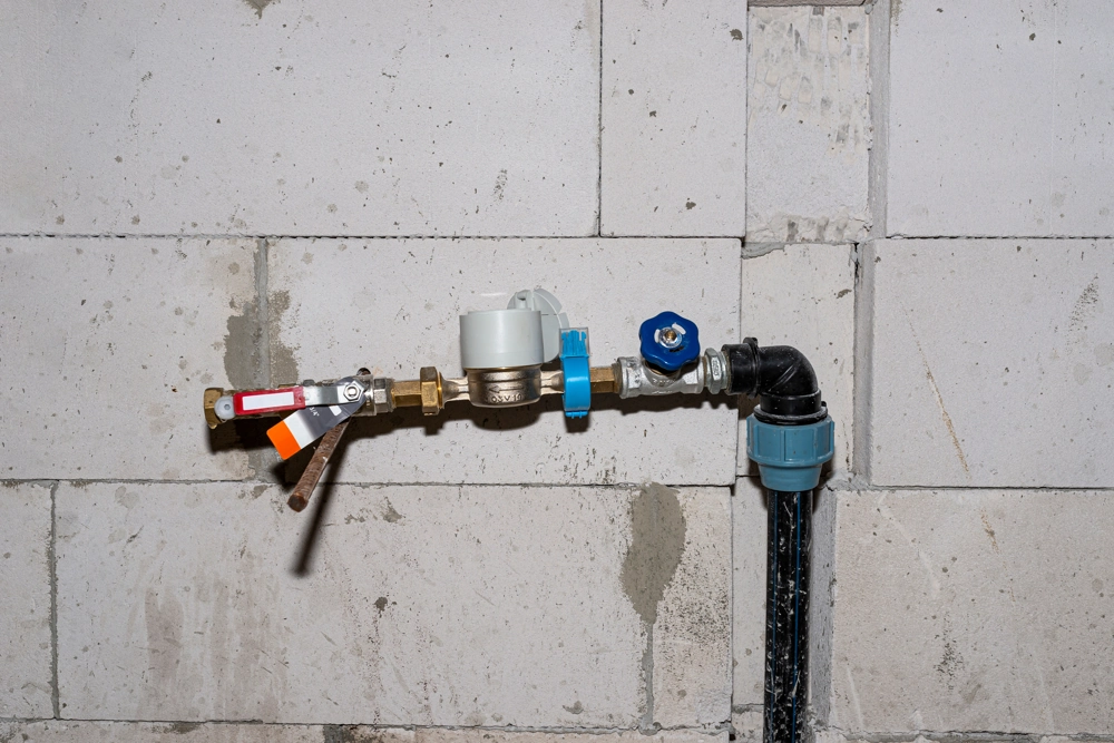 Sanitärinstallation mit Wasserzähler, Absperrventilen und Rohrleitung an roher Mauerwerkswand