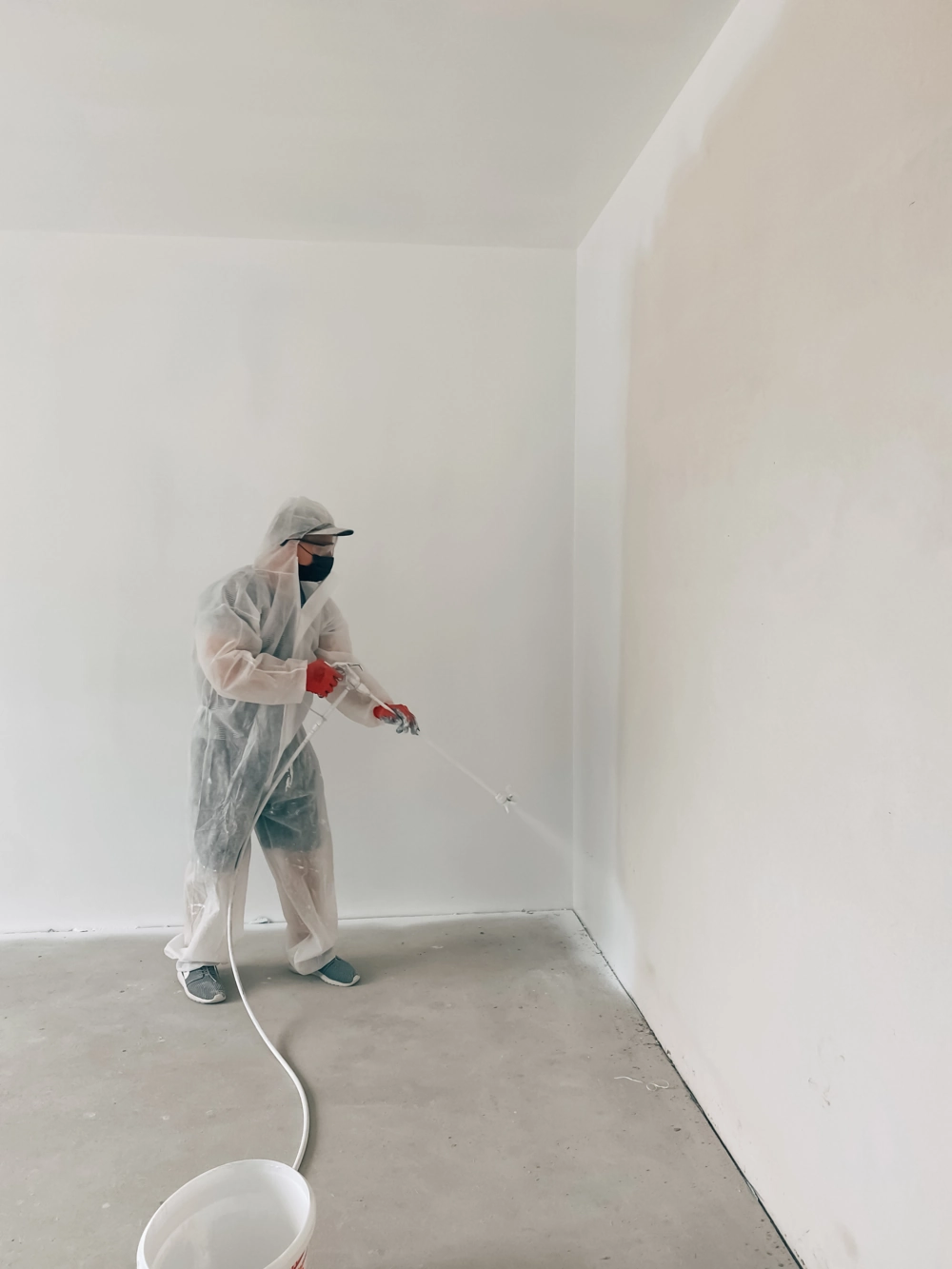 Handwerker trägt Spritzspachtel mit Spritzpistole auf Innenwand auf